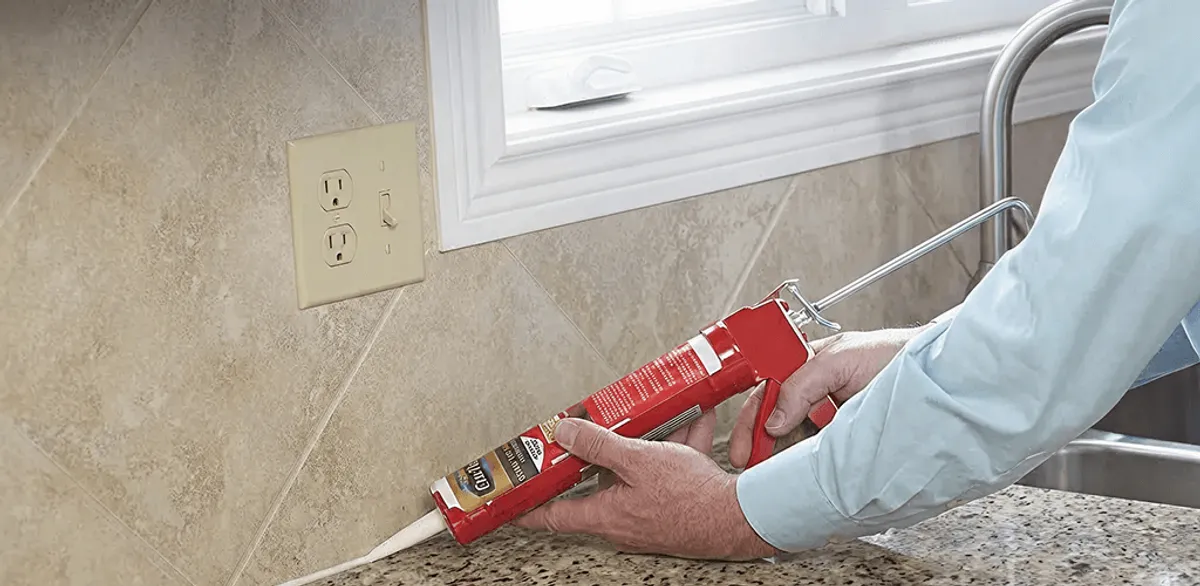 Handyman applying caulk along a kitchen backsplash and countertop seam in Dover, DE