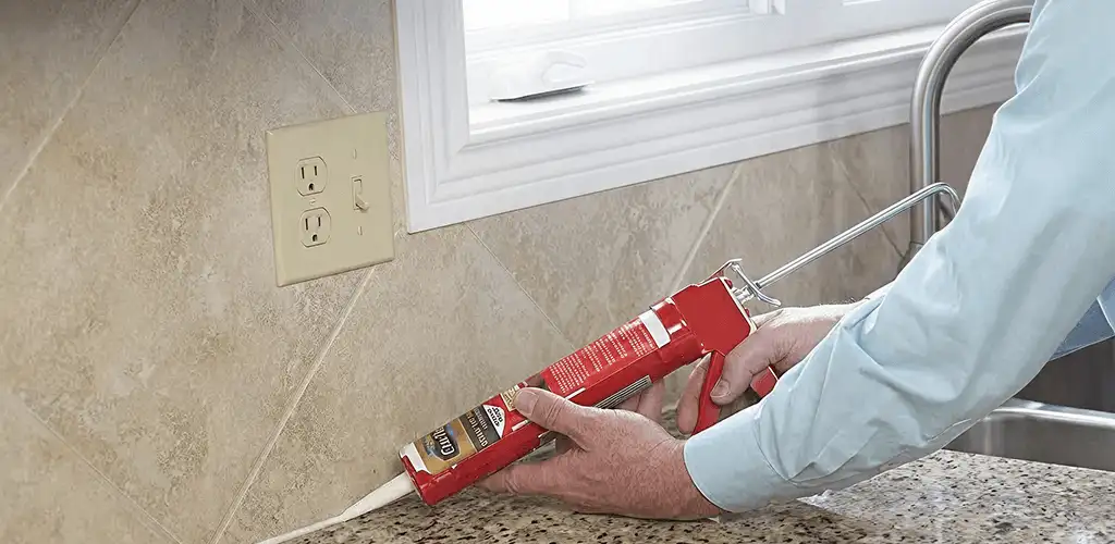 Handyman applying caulk along a kitchen backsplash and countertop seam in Dover, DE